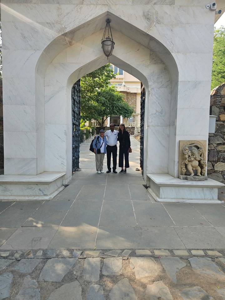 Three travellers stand together beneath a grand white-marble gateway in a palace courtyard.