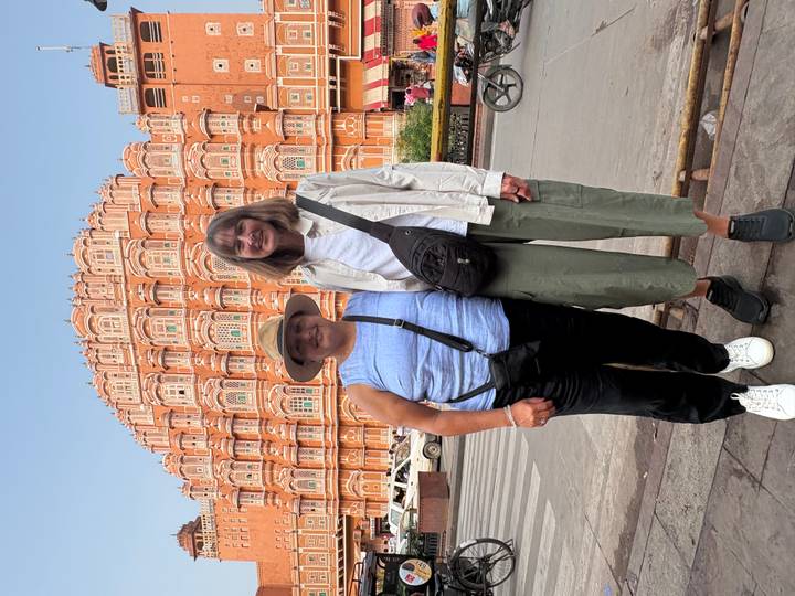 Two women posing in front of Jaipur’s pink Hawa Mahal on a sunny day.
