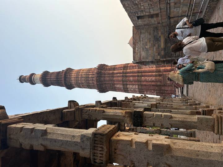 Towering red sandstone Qutub Minar surrounded by historic archways and visitors.