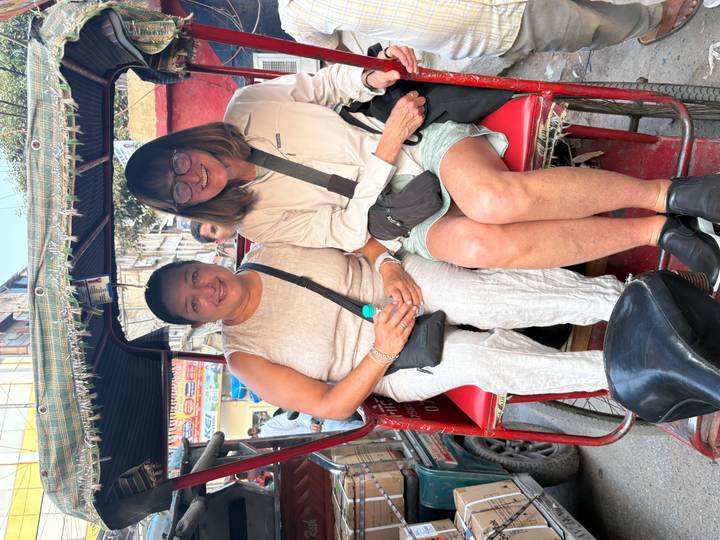 Two women seated in a cycle rickshaw navigating lively city streets.