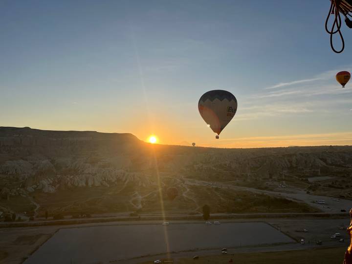 Silhouetted balloon floats past the rising sun above Cappadocia’s otherworldly terrain.