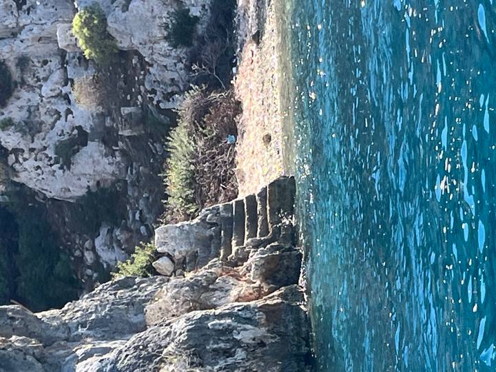 Stone steps carved into a rocky shoreline descend into clear blue water.