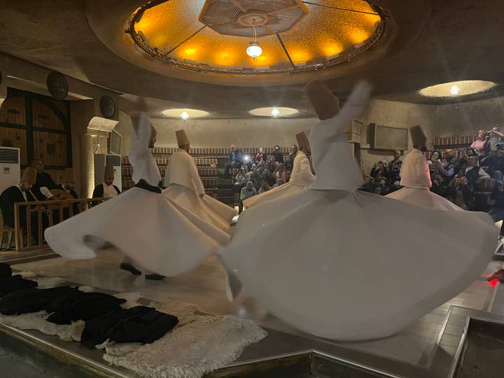 Whirling dervishes in flowing white robes spin in a softly lit cultural performance hall.