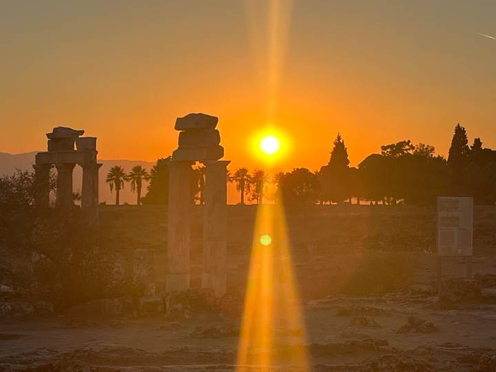 Silhouetted ancient columns and palm trees against a golden sunset.