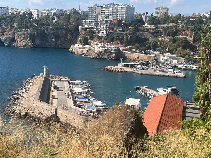 Clifftop view of a harbor with boats, breakwater and deep blue sea below.