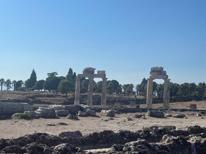 Four standing stone columns amid scattered ruins under a clear blue sky.