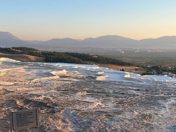 Expansive white travertine terraces of Pamukkale glowing in late afternoon light with distant mountains.