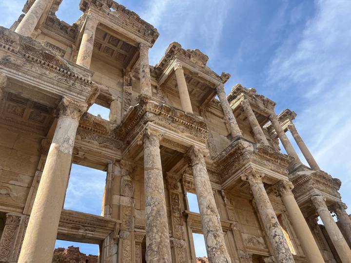 Upward view of the ornate façade of the Library of Celsus under a lightly clouded sky.