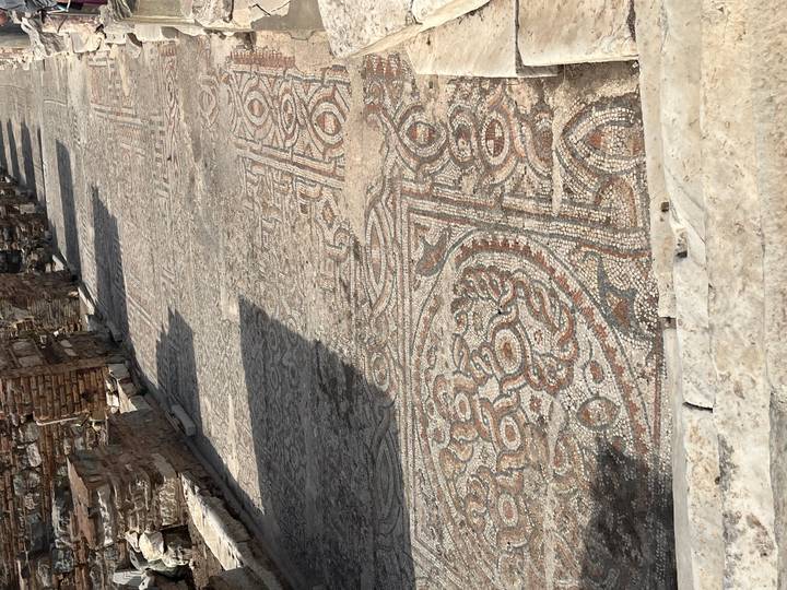 Section of ancient mosaic pavement with geometric and floral patterns in sun and shadow.