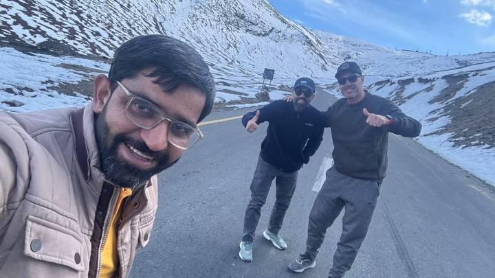 Selfie of three friends on a snowy mountain road smiling and gesturing cheerfully.