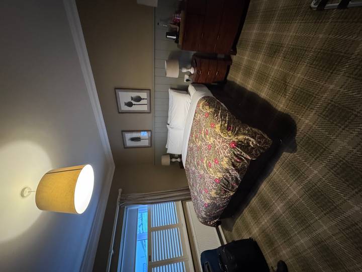 Cozy hotel bedroom with patterned duvet, plaid carpet and warm lamp lighting.