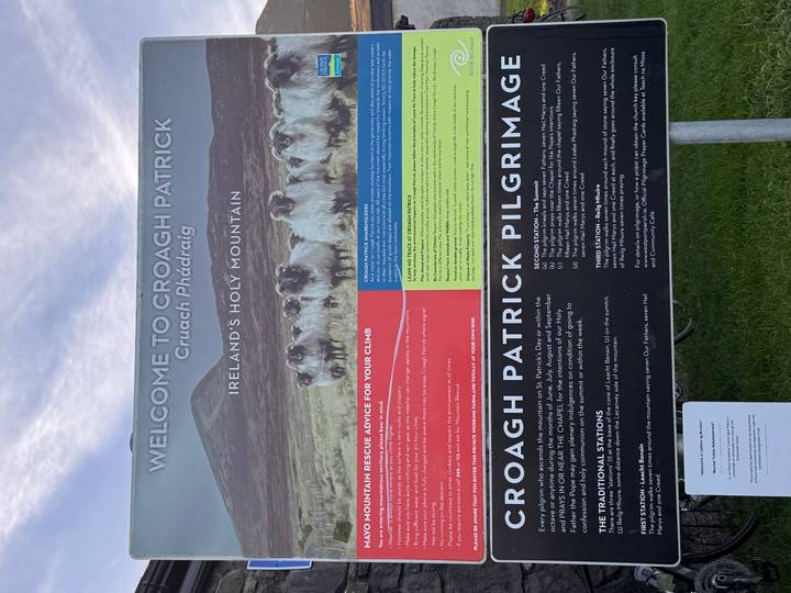 Visitor information board welcoming climbers to Croagh Patrick, set against grassy hillside.