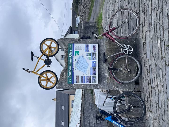 Outdoor stone plinth holding a bicycle and a detailed tourist map of Inis Oírr island with photos.