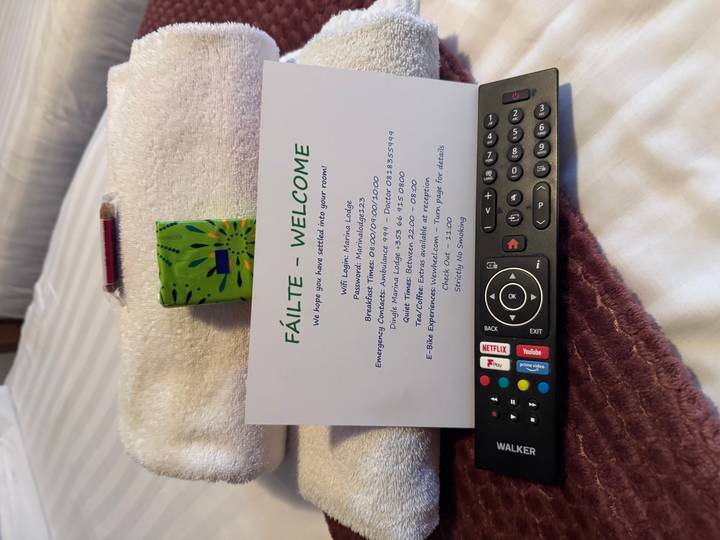 Welcome card, TV remote and towel arranged on a hotel bed.