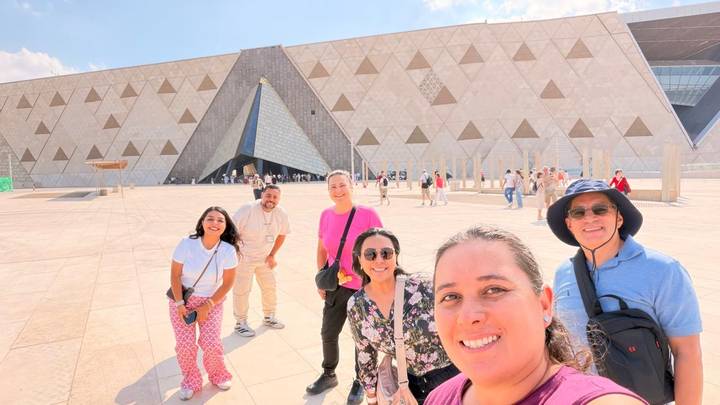 Smiling travelers take a selfie outside the geometric façade of Egypt’s Grand Museum.