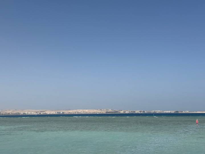 Calm turquoise waters of the Red Sea stretch toward a distant desert shoreline under a clear sky.