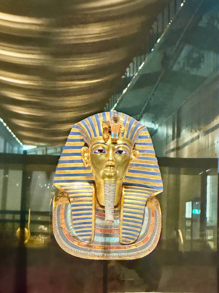 Iconic gold funerary mask of Tutankhamun shines under museum lights.