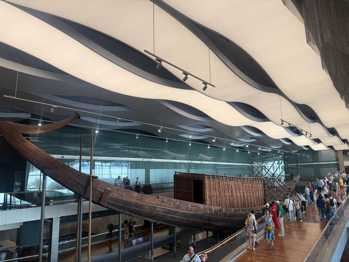Museum hall exhibits the restored ancient wooden solar boat beneath wave-like ceiling panels.
