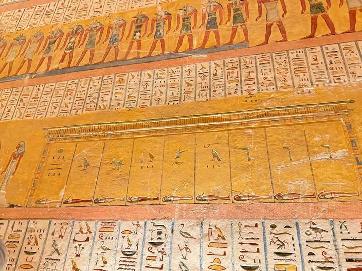 Detailed golden wall friezes and hieroglyphs adorn an ancient Egyptian burial chamber.