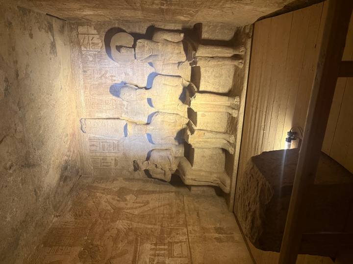 Dim interior chamber of Abu Simbel displays seated carved figures illuminated by spotlight.