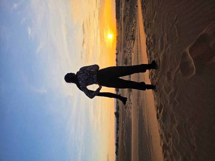 Silhouette of a traveler standing on golden sand dunes watching the sun set over the Sahara.