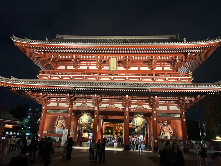 Grand red Kaminarimon gate of Senso-ji temple brightly lit at night with visitors below.