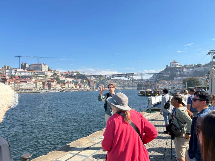 Tour guide speaks to a group along the river with the Dom Luís I Bridge and Porto skyline behind
