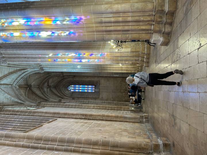 Visitor walking inside a soaring Gothic cathedral lit by colourful stained-glass reflections