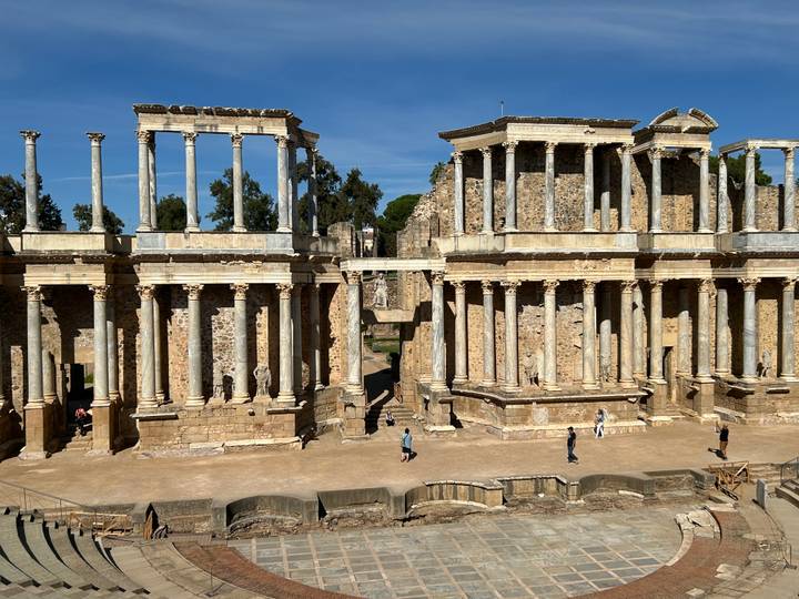 Wide view of the well-preserved Roman theatre with colonnaded stage and people exploring the site