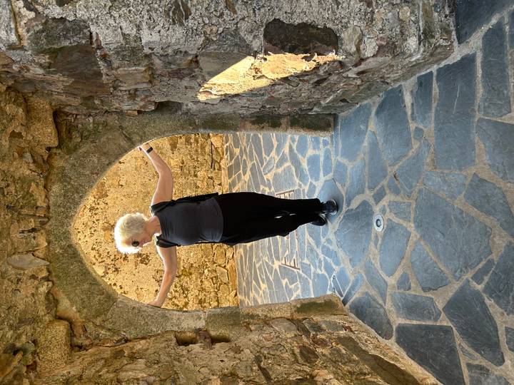 Woman posing playfully under a small stone archway inside a medieval castle ruin