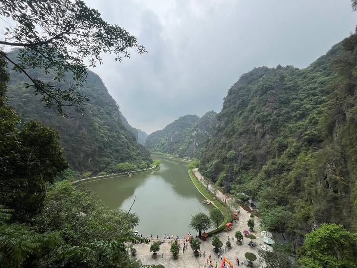 A winding green river cuts through steep, forested karst cliffs under an overcast sky, creating a tranquil valley panorama.