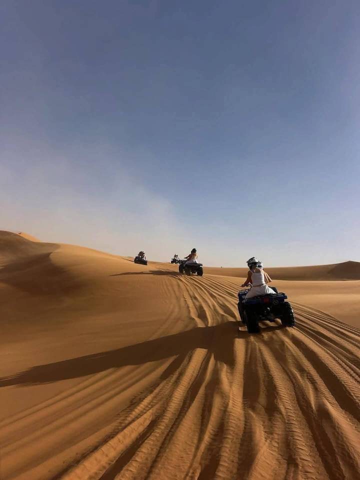 Travellers riding quad bikes across golden desert dunes leaving sweeping tracks