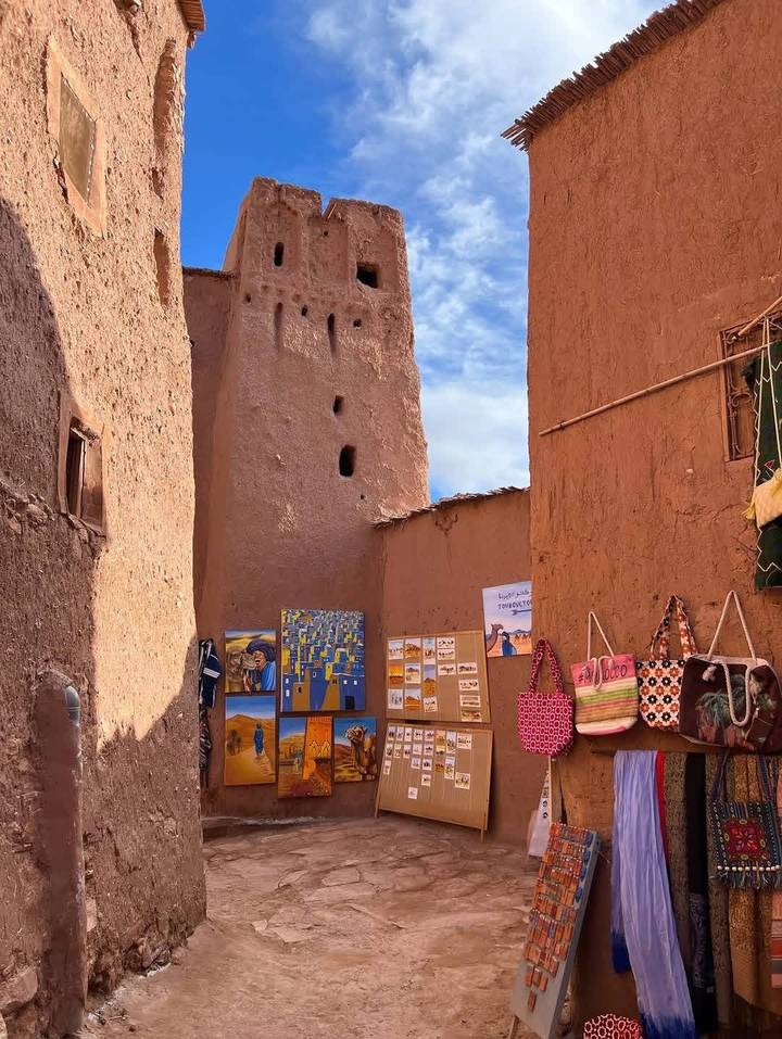 Adobe alleyway lined with colourful local crafts near an ancient mud-brick tower