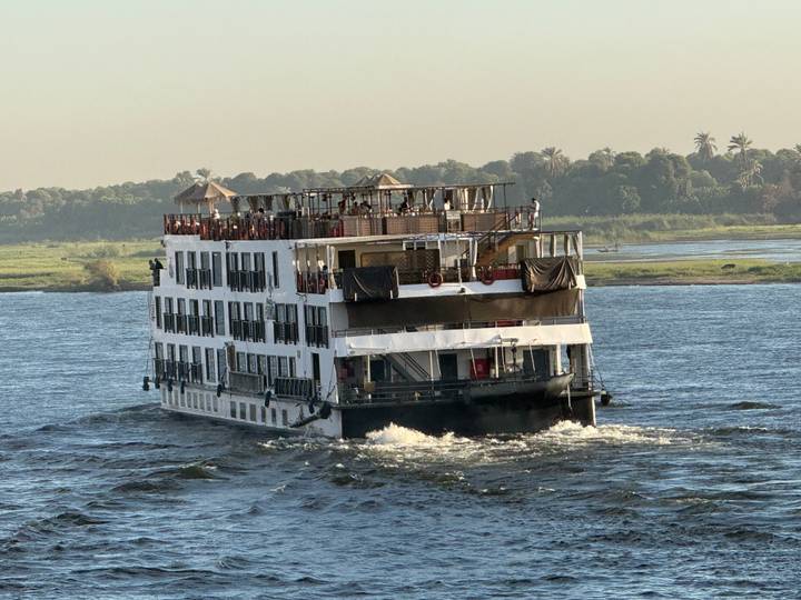 White multi-deck Nile cruise ship sailing upstream at sunset