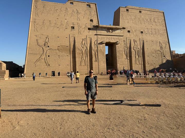 Visitor standing in front of monumental Edfu Temple gate adorned with reliefs