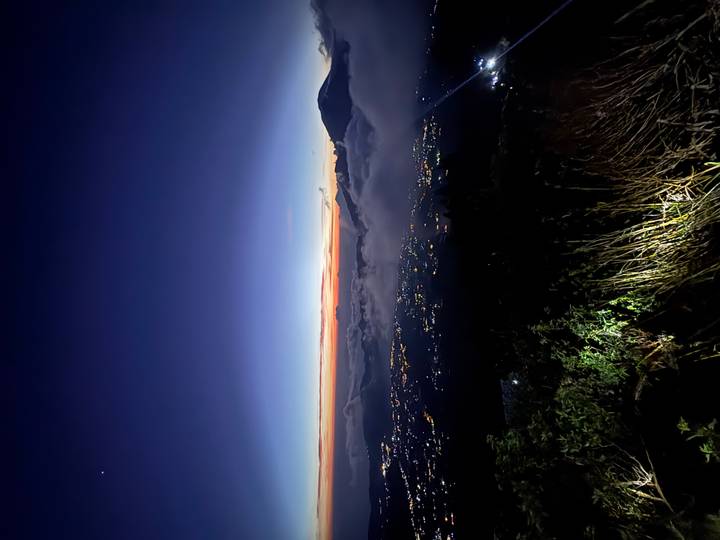 Pre-dawn panorama from a mountain viewpoint showing city lights beneath layers of mist and a colorful horizon.