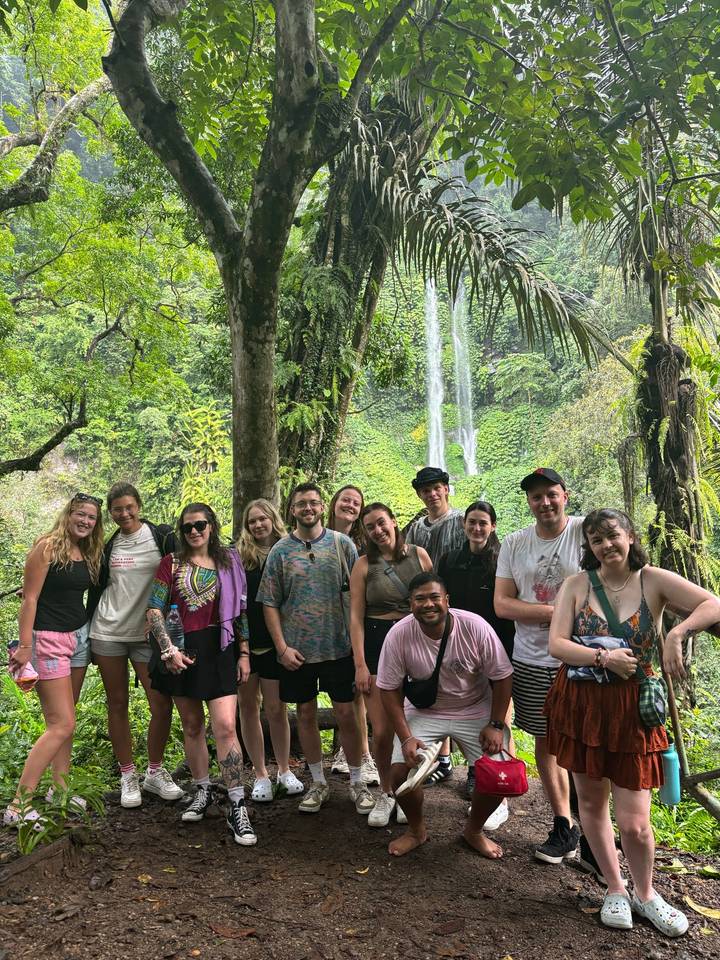 Group of travelers posing in front of a tall jungle waterfall surrounded by lush greenery.