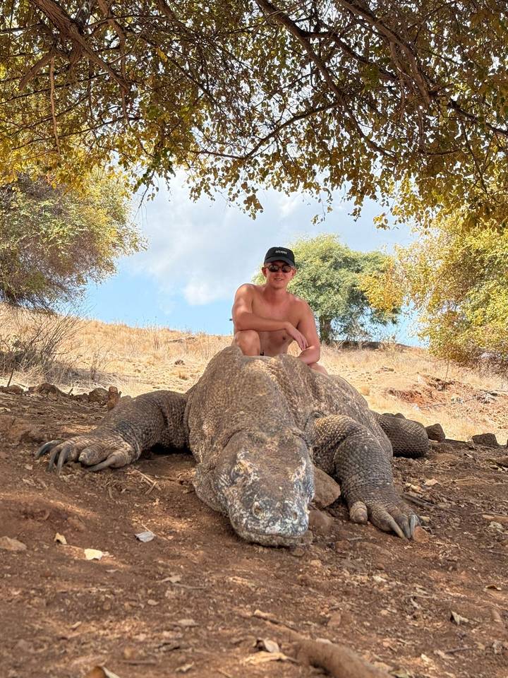 Traveler crouching behind a massive Komodo dragon in a dry savanna landscape.