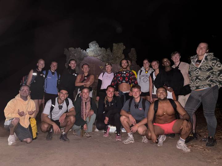 Large hiking group poses at night with head-torches near a rocky formation.
