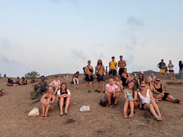 Travelers sit on a dry hillside waiting for sunset with hazy sky overhead.
