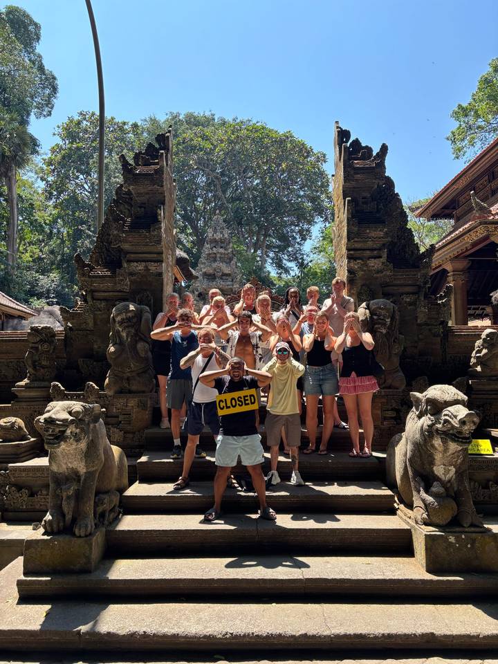 Group copies the hear-no-evil monkey pose at an ornate stone temple entrance filled with carvings.
