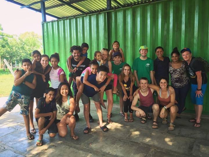 Group of people posing in front of a green structure.