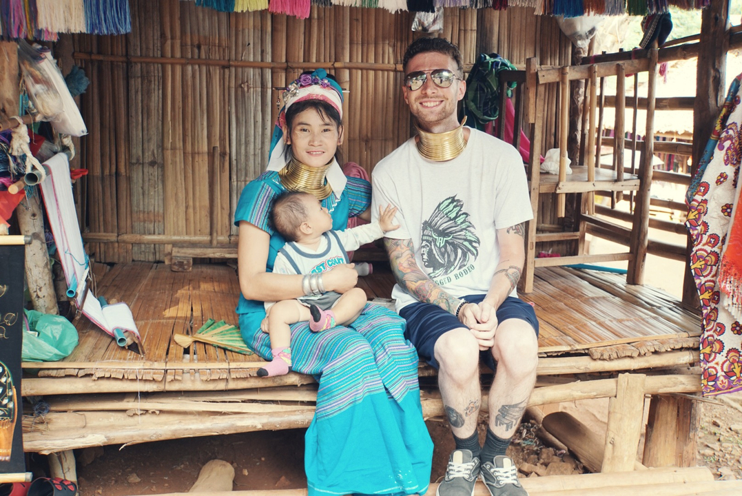 Homme accompagné d'une femme locale et d'un bébé, assis en tenue traditionnelle.