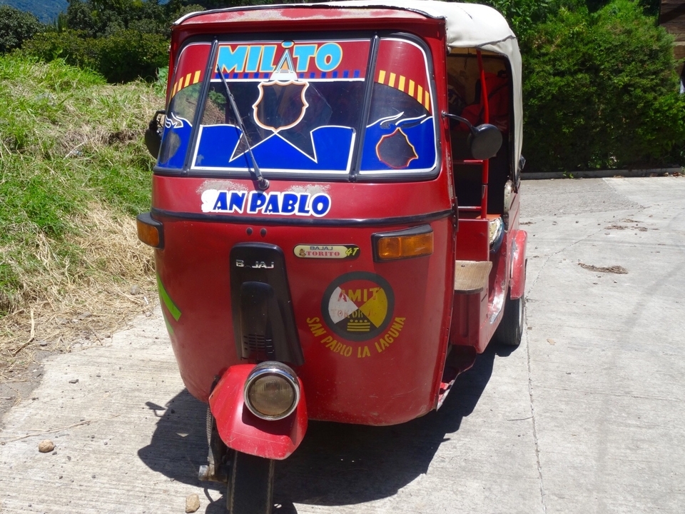 Un tuk-tuk motorisé garé sur une route en béton.