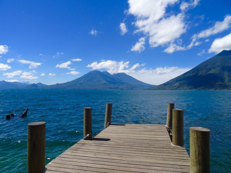 Un quai se prolongeant dans un lac bleu clair avec des montagnes.
