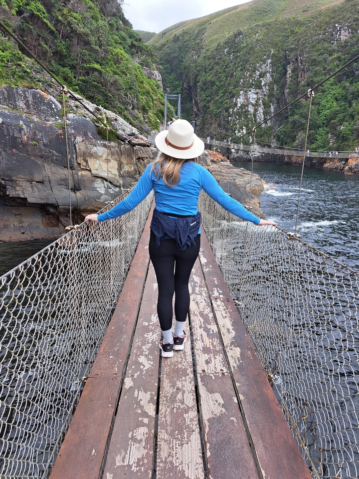 Person on a suspension bridge over a rocky river.