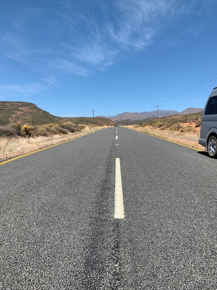 Empty road leading through a mountainous landscape with a van parked on the side.