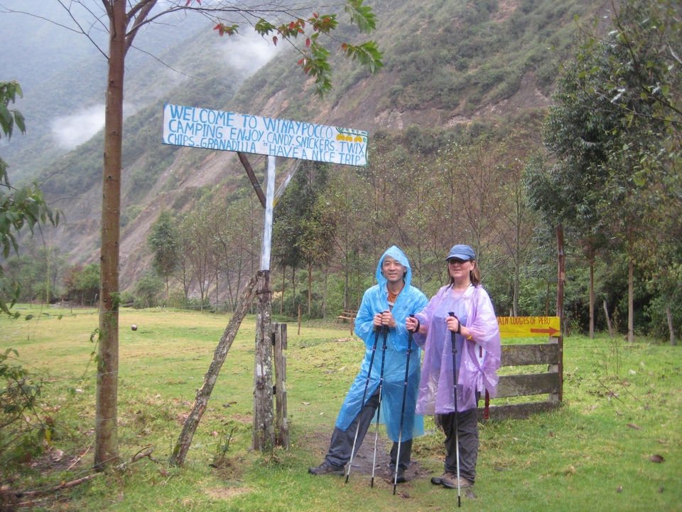 Deux personnes en ponchos de pluie devant un panneau de départ de sentier.