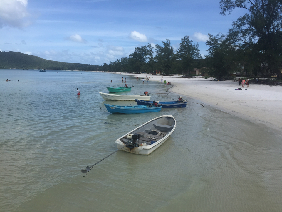 Boats moored on a sandy beach with people swimming.