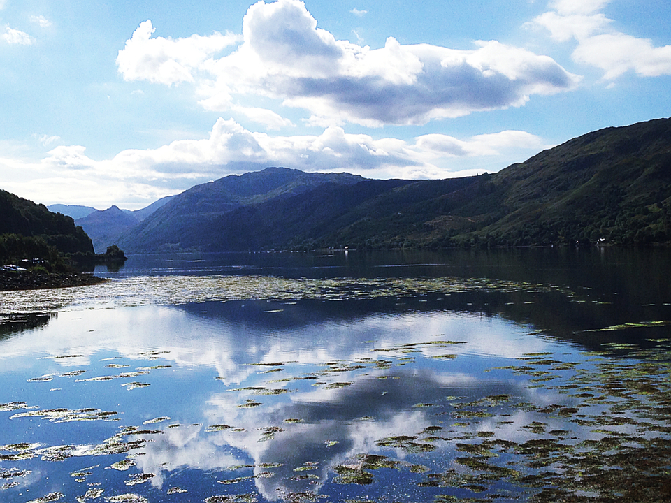 Tranquil lake surrounded by lush hills and blue skies.